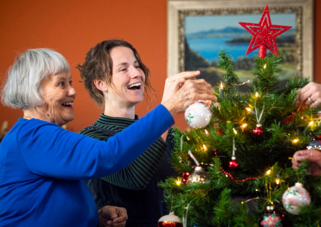 Women hanging baubles on hospice Remembrance Tree